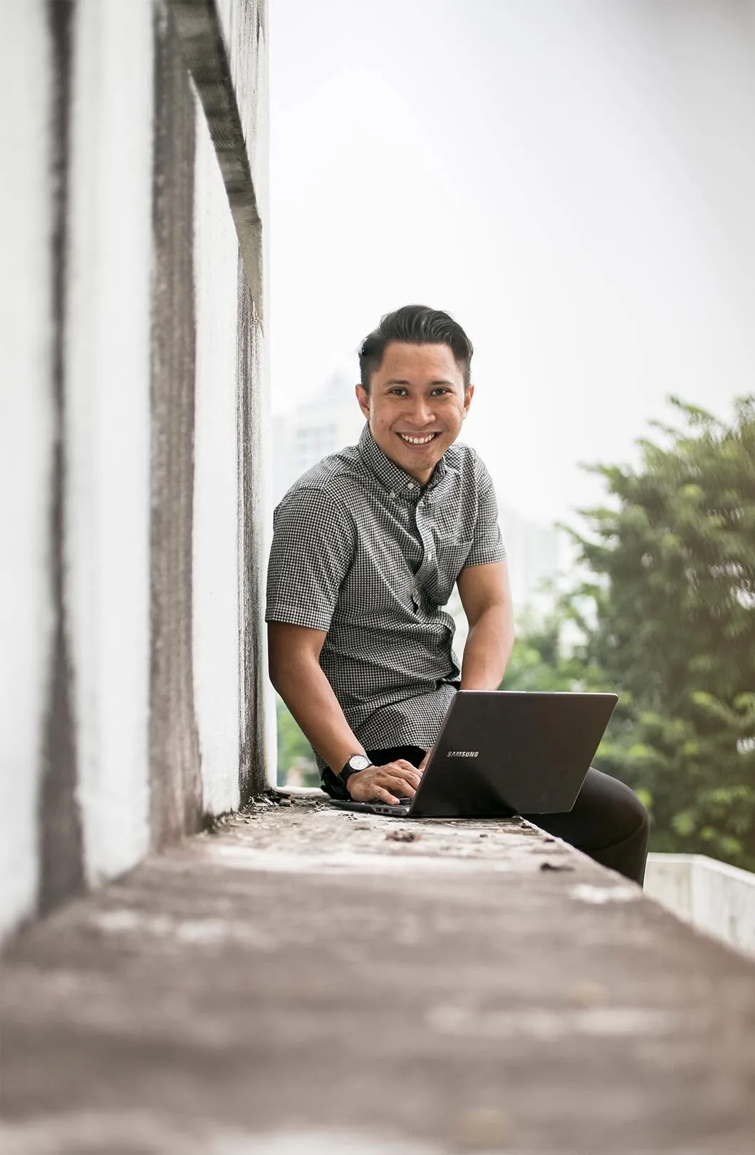Nazreen Daud smiling beside his laptop on a ledge, one of the first photos from the start of his laptop-based career