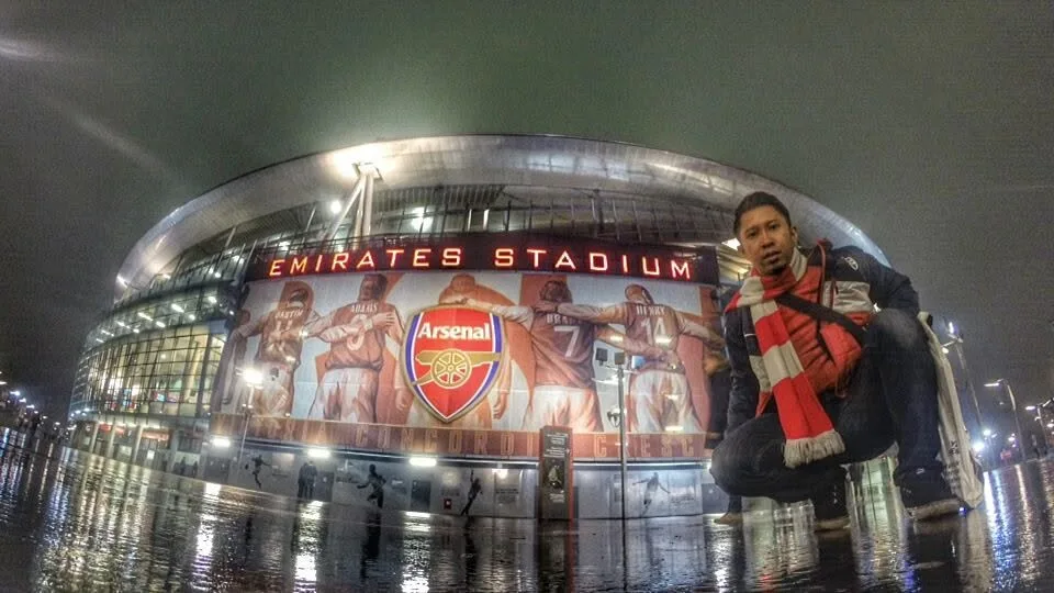 Nazreen Daud in an Arsenal scarf outside the Emirates Stadium in London at night, on his first visit