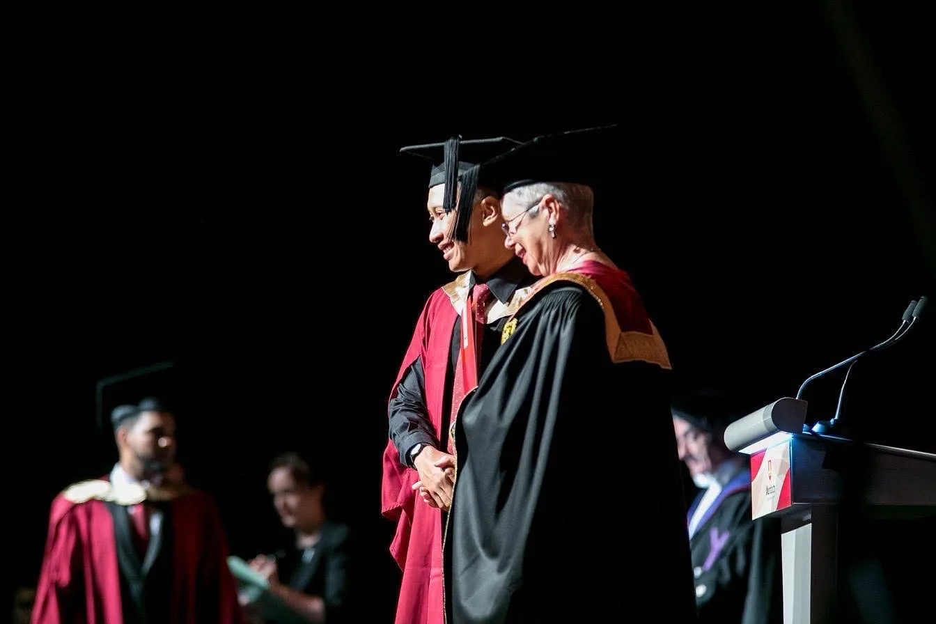 Nazreen Daud on stage in a red academic gown and mortarboard at his Murdoch University degree convocation