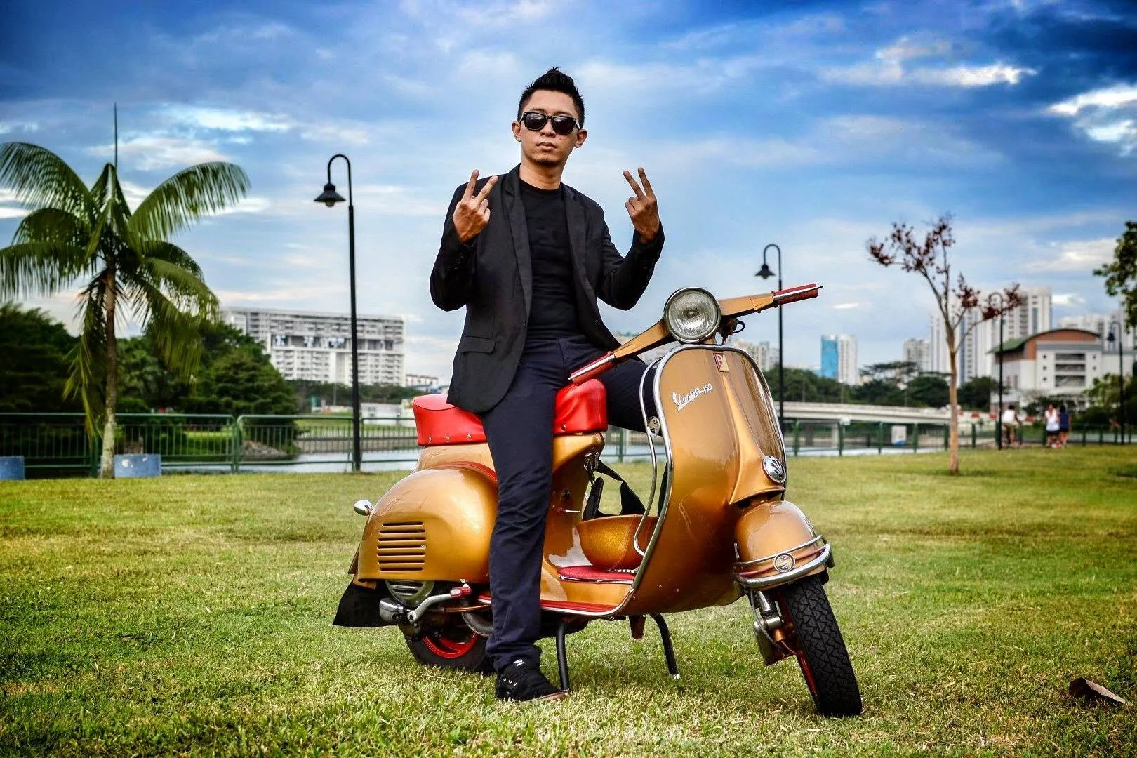 Nazreen Daud sitting on his gold Iron Man-inspired Vespa in a park, making peace signs