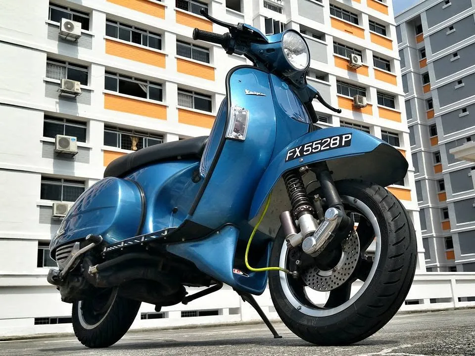 Close-up of Nazreen Daud's blue Vespa PX 200, showing the front disc brake and suspension
