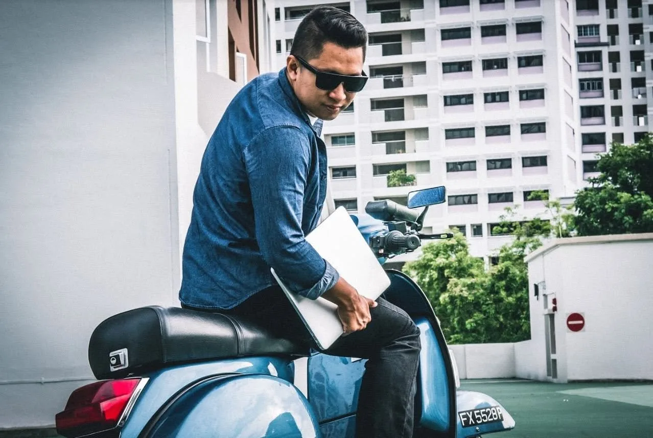 Nazreen Daud sitting on his blue Vespa PX 200, holding a laptop