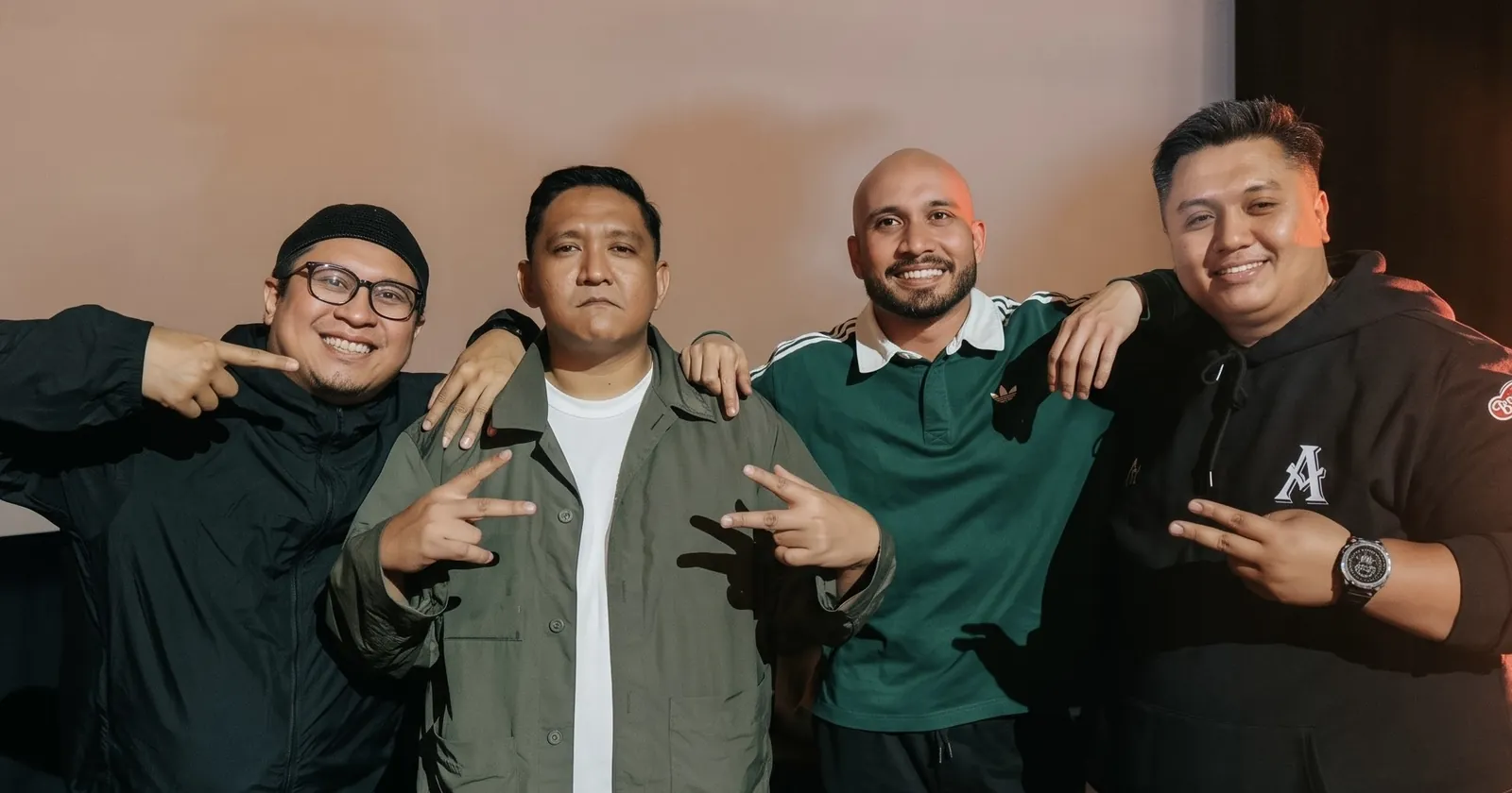 Four men smiling and making peace-sign hand gestures together in front of a projection screen